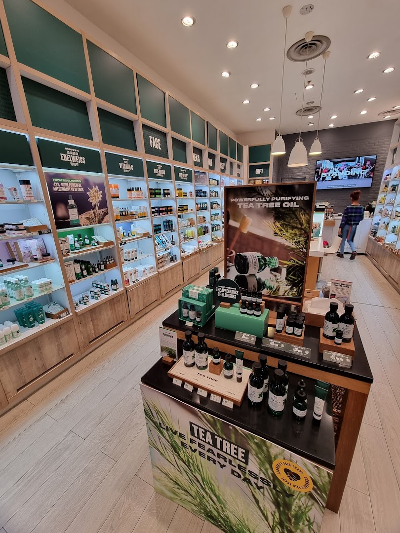 An interior view of The Body Shop, showcasing skincare products on well-lit shelves and a prominent Tea Tree Oil display.