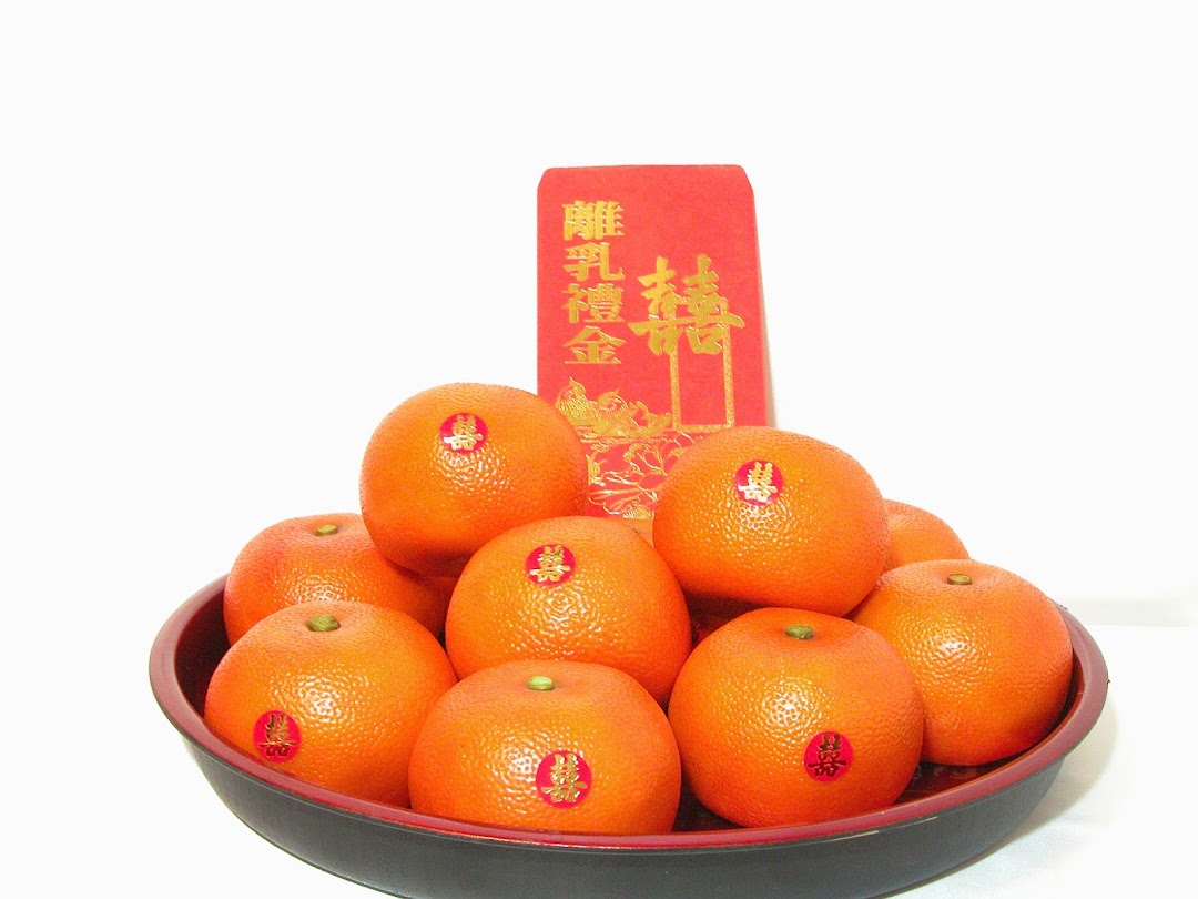A bowl of oranges with double happiness stickers and a red packet, symbolizing good fortune.