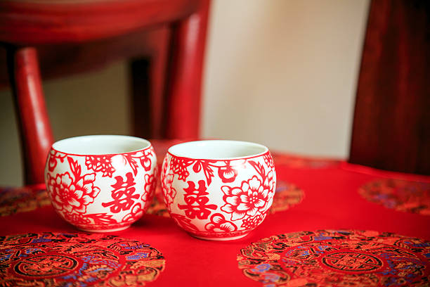 Two traditional Chinese wedding tea cups with "double happiness" characters on a red patterned cloth.