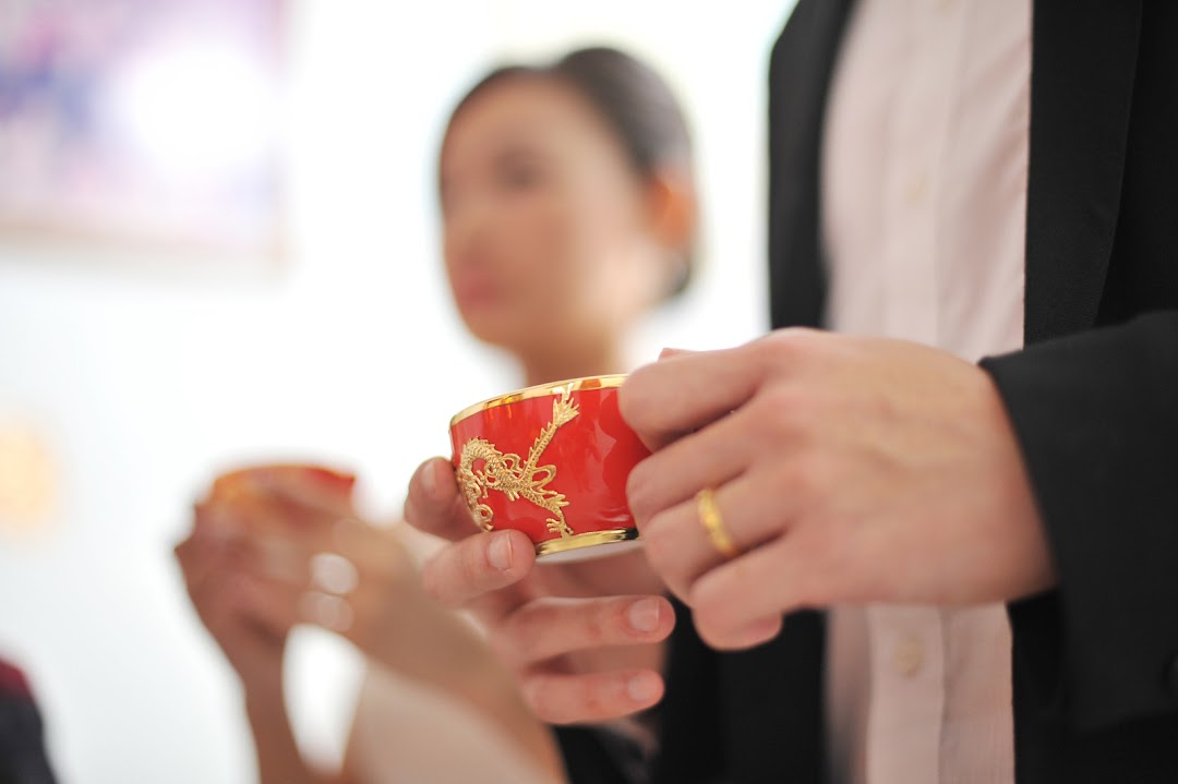 A close-up of hands holding a traditional red and gold cup, likely for a Chinese wedding tea ceremony.
