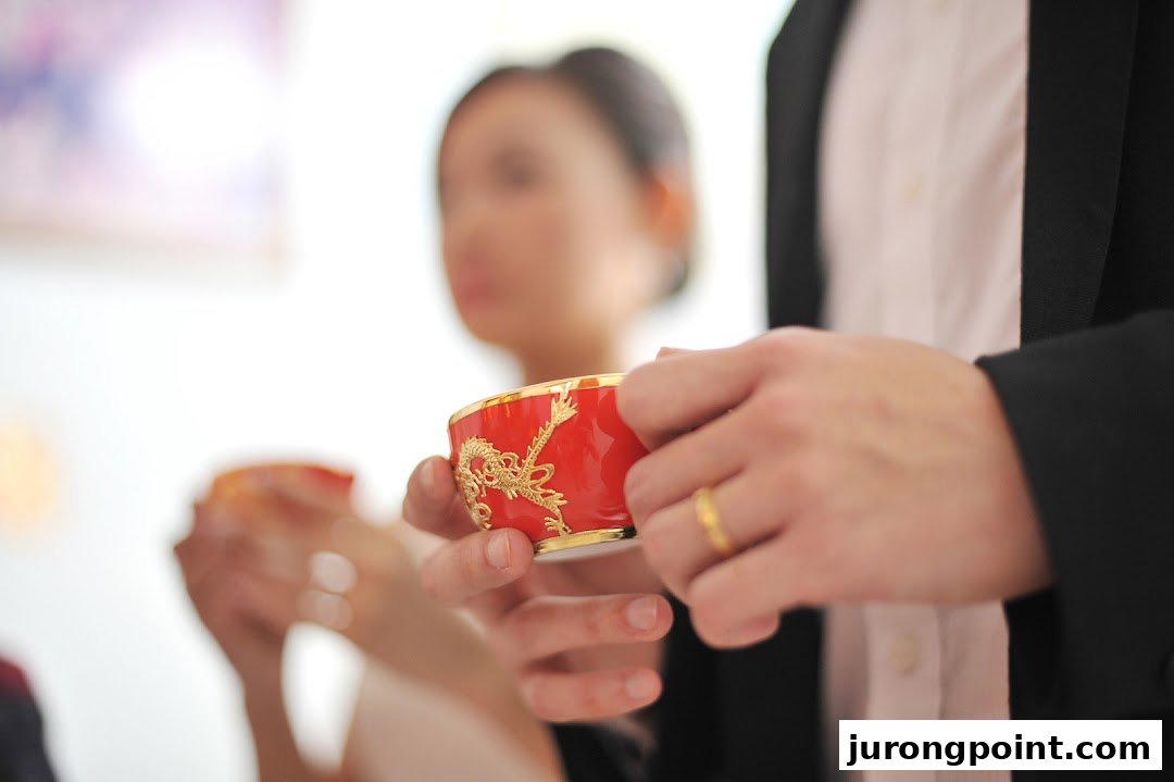 A close-up of hands holding a traditional red and gold cup, likely for a Chinese wedding tea ceremony.