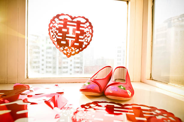 Red embroidered wedding shoes and double happiness decor by a window, symbolizing Chinese wedding traditions.