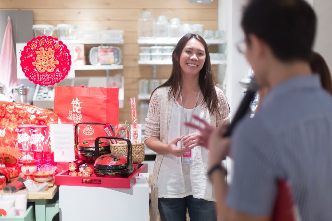 A smiling staff member stands by a vibrant display of traditional Chinese wedding essentials and gifts.