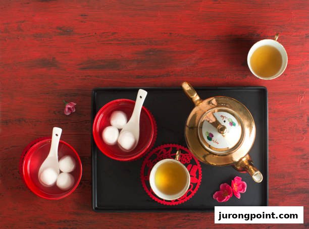 Overhead view of traditional Chinese tangyuan and a golden tea set on a black tray against a red background.