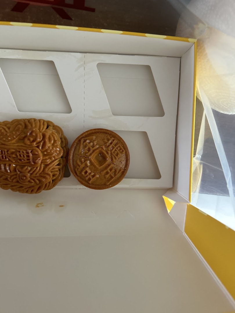 Two traditional Chinese pastries, possibly mooncakes, in a white and yellow gift box.