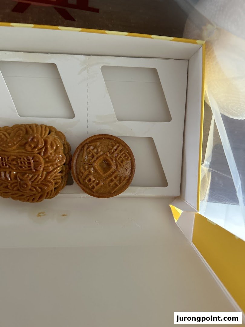 Two traditional Chinese pastries, possibly mooncakes, in a white and yellow gift box.
