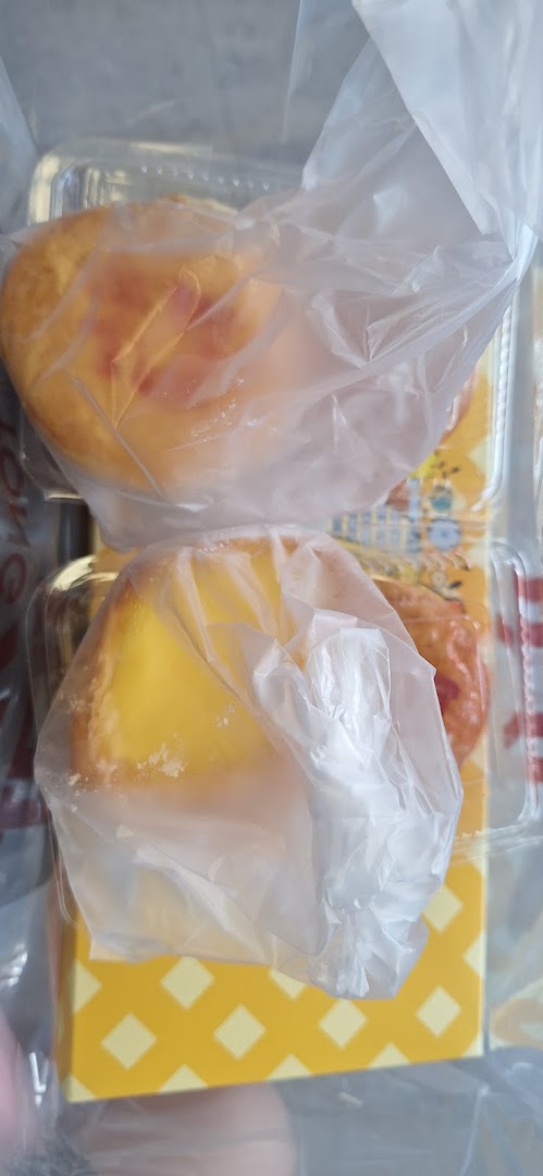 Two golden pastries, likely egg tarts, individually wrapped in plastic and presented in a patterned box.
