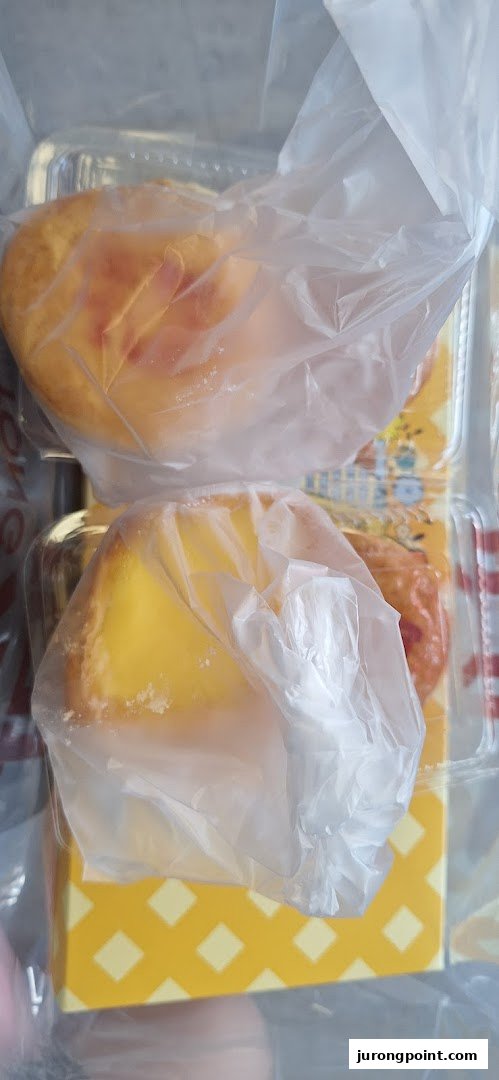 Two golden pastries, likely egg tarts, individually wrapped in plastic and presented in a patterned box.