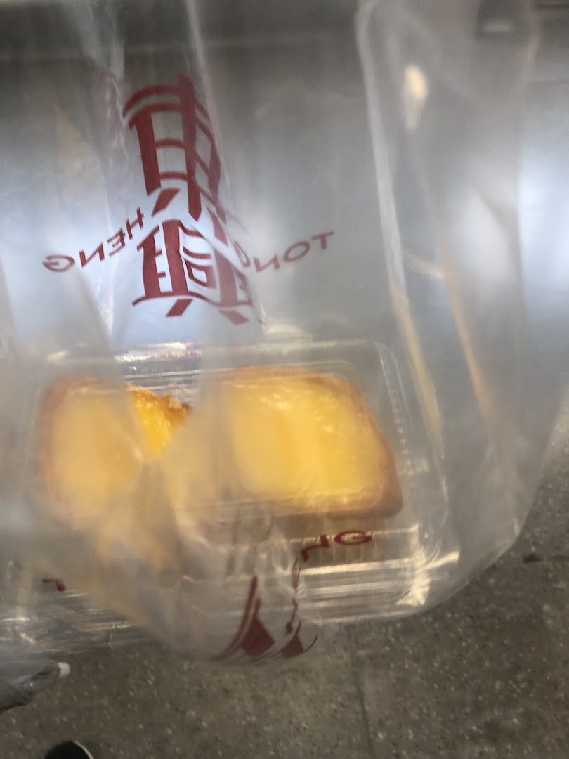 Two golden pastries in a clear container inside a Tong Heng branded plastic bag.