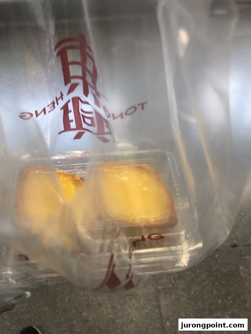 Two golden pastries in a clear container inside a Tong Heng branded plastic bag.