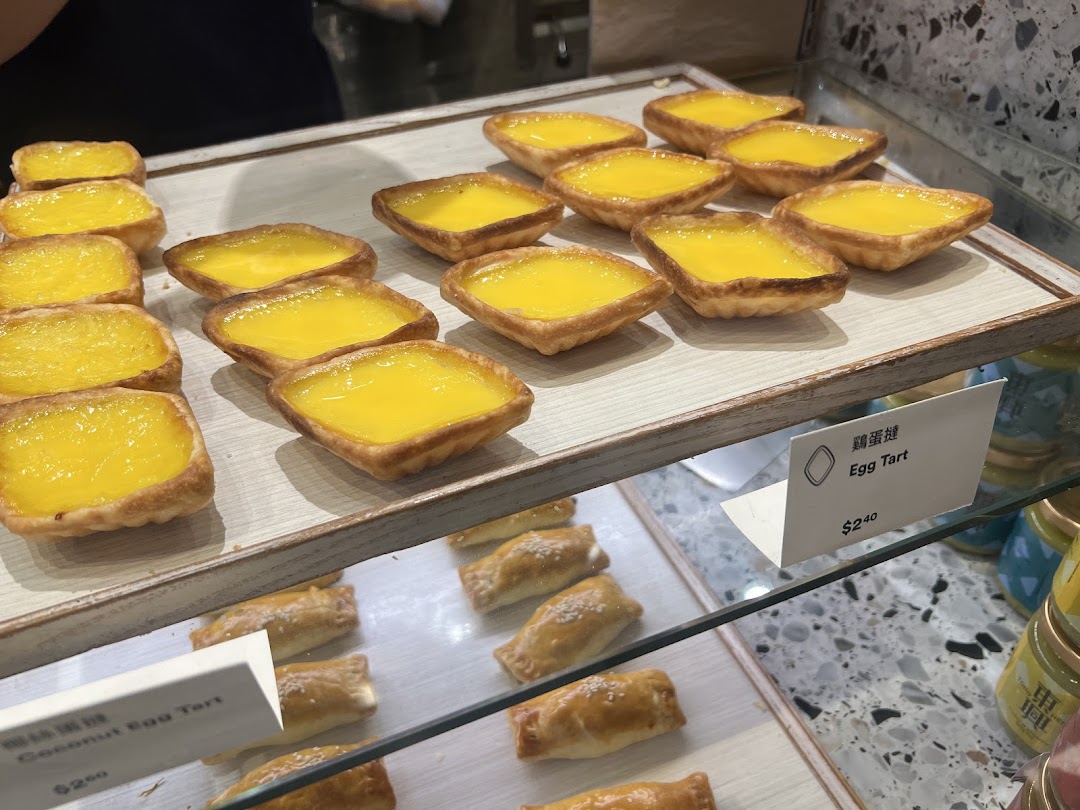 A close-up view of freshly baked golden egg tarts and other pastries displayed in a bakery.