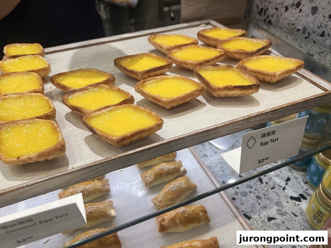 A close-up view of freshly baked golden egg tarts and other pastries displayed in a bakery.