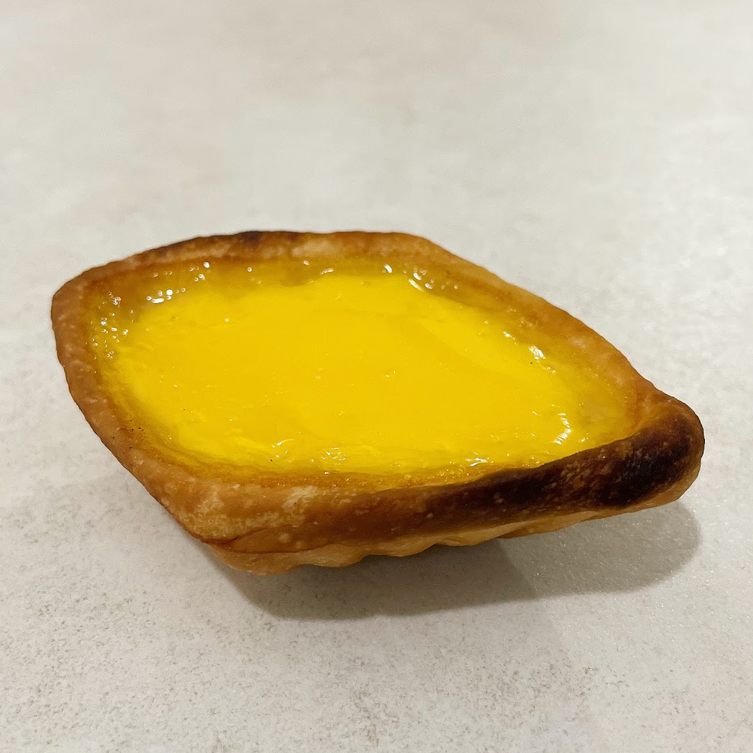 A close-up of a golden-yellow egg tart with a flaky crust from Tong Heng.