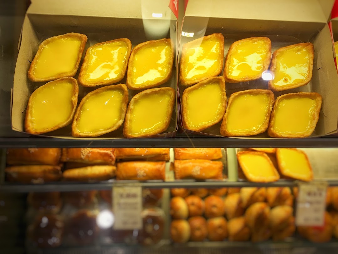 Close-up of golden diamond-shaped egg tarts and other pastries displayed in a glass case.