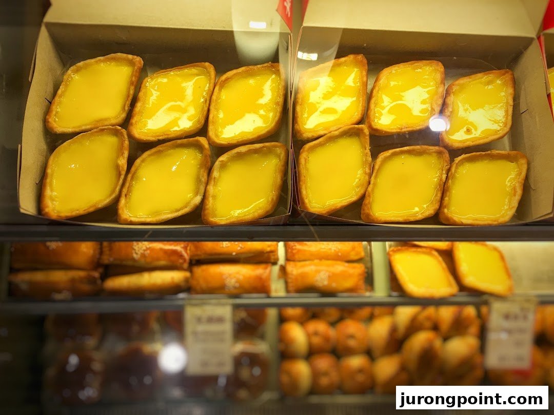 Close-up of golden diamond-shaped egg tarts and other pastries displayed in a glass case.