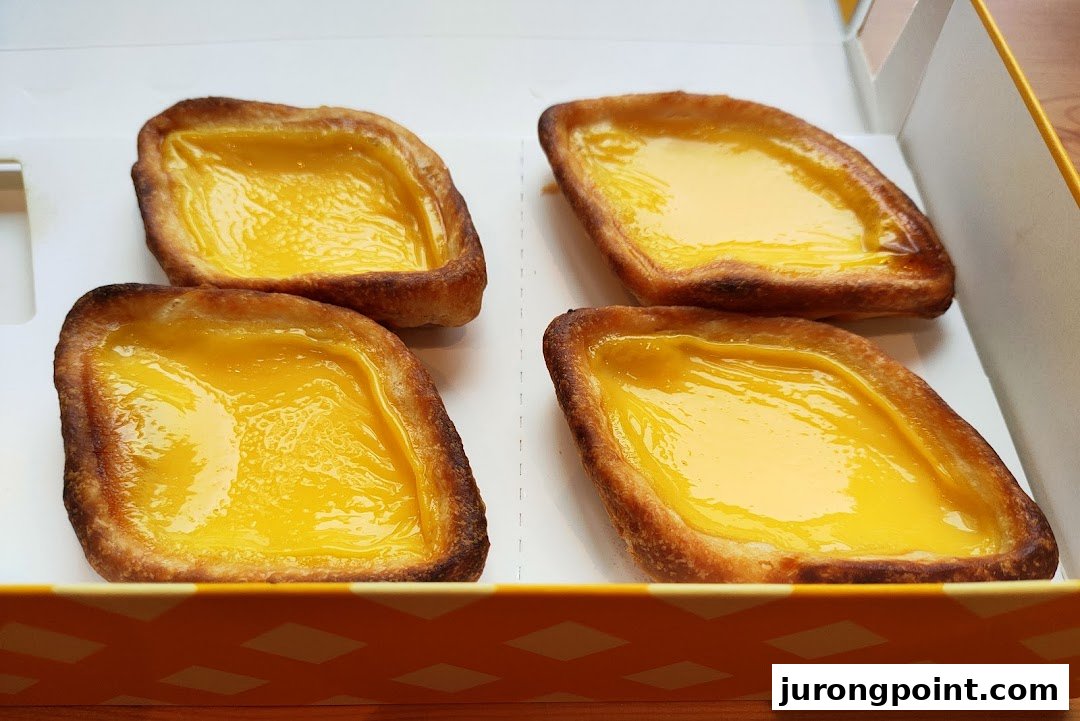 Four signature diamond-shaped egg tarts with golden custard in a Tong Heng takeaway box.