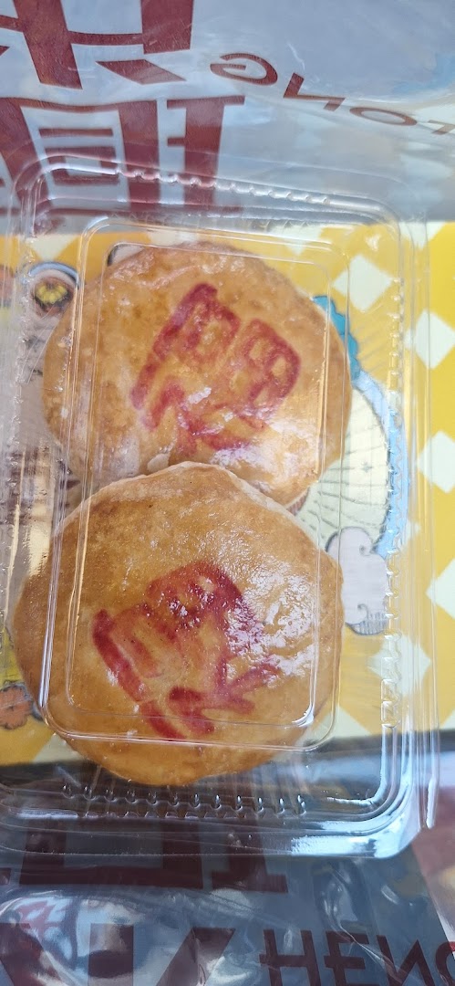 Two golden-brown traditional Chinese pastries with red auspicious characters, packaged in a clear plastic container.