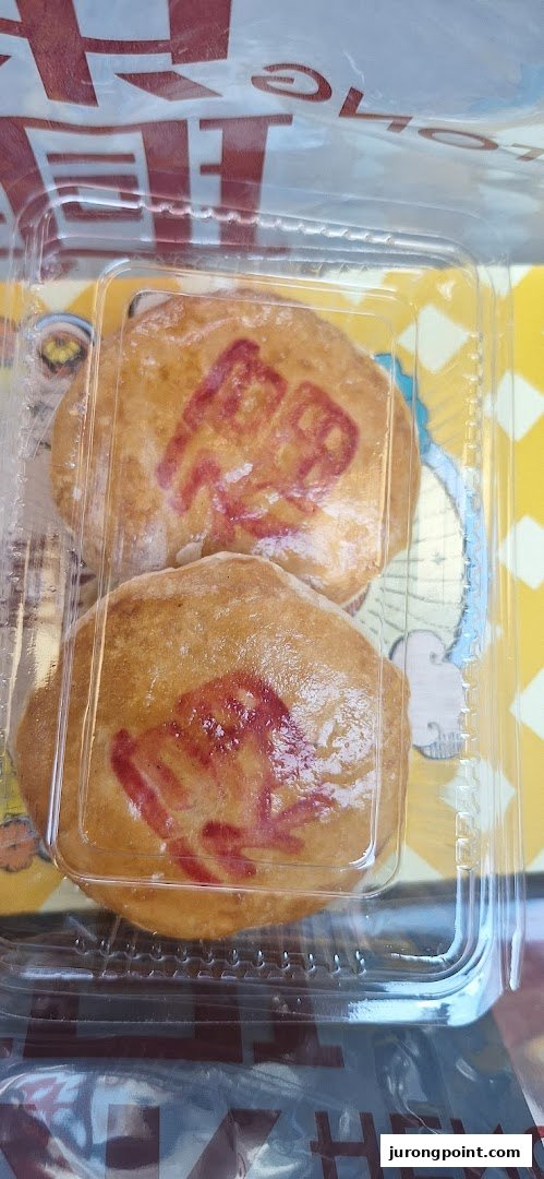 Two golden-brown traditional Chinese pastries with red auspicious characters, packaged in a clear plastic container.