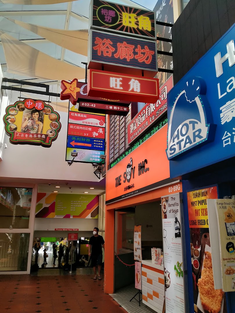 A vibrant mall walkway featuring diverse shop fronts including The Soy Inc. and Hot Star Large Fried Chicken.