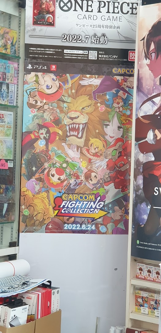 Promotional posters for One Piece Card Game and Capcom Fighting Collection displayed inside a game store.