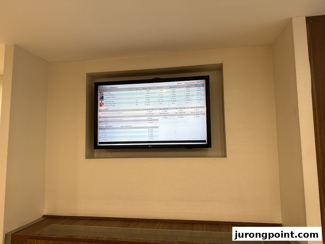 A digital display inside a bank branch showing foreign currency exchange rates and account information.