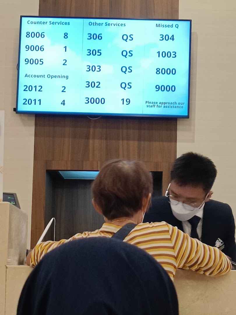 A customer interacts with staff at UOB Bank, with a queue number display visible.