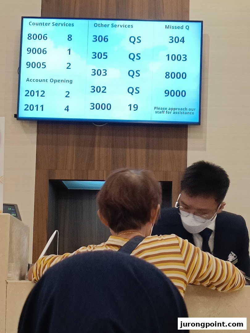 A customer interacts with staff at UOB Bank, with a queue number display visible.