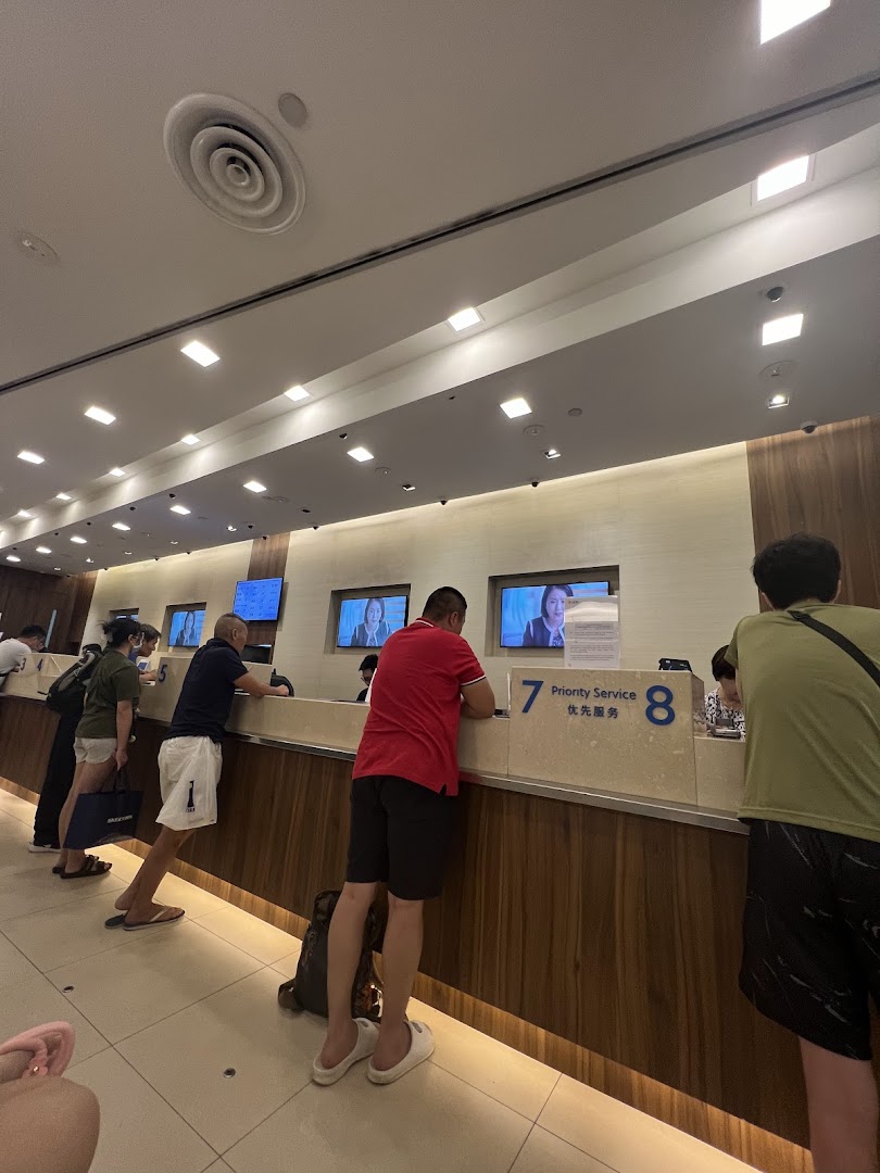 Customers are seen at service counters inside the UOB bank branch, with screens displaying information.