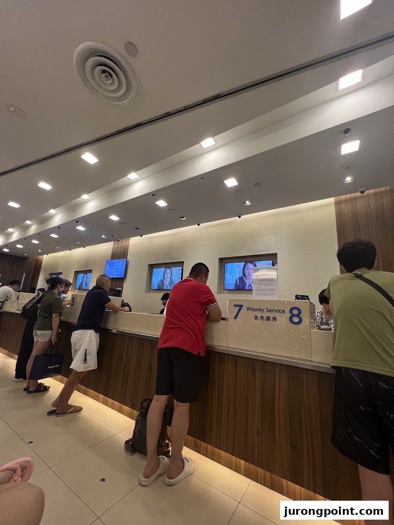 Customers are seen at service counters inside the UOB bank branch, with screens displaying information.