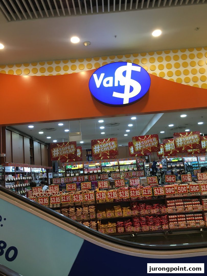 View of Valu shop entrance with its distinctive logo and shelves filled with discounted products, seen from an escalator.