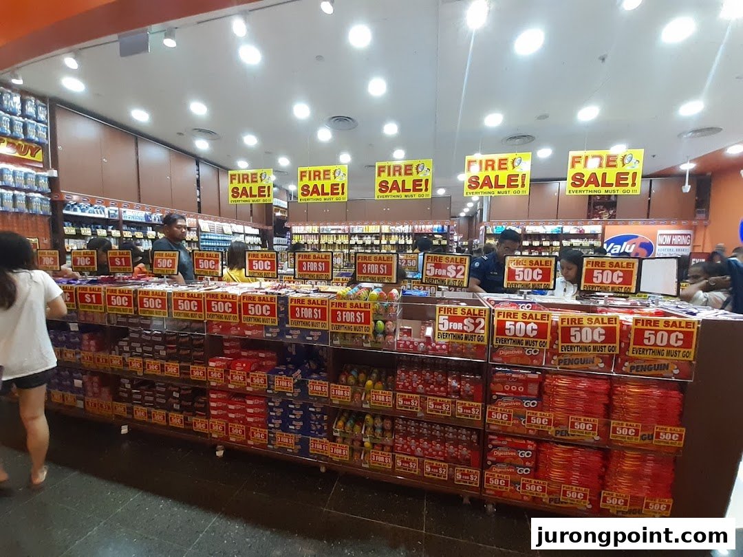Interior view of Valu store showcasing a "Fire Sale" with various discounted products and shoppers.