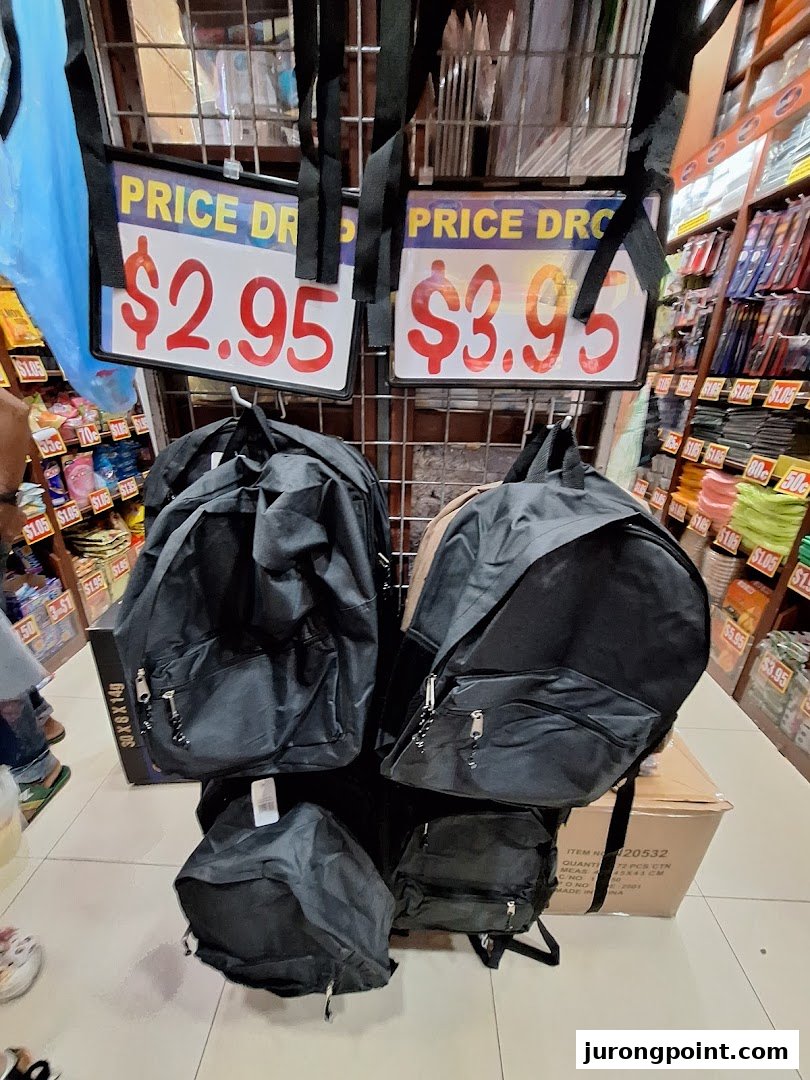 Black backpacks displayed for sale with 'Price Drop' signs at $2.95 and $3.95 in a retail store.