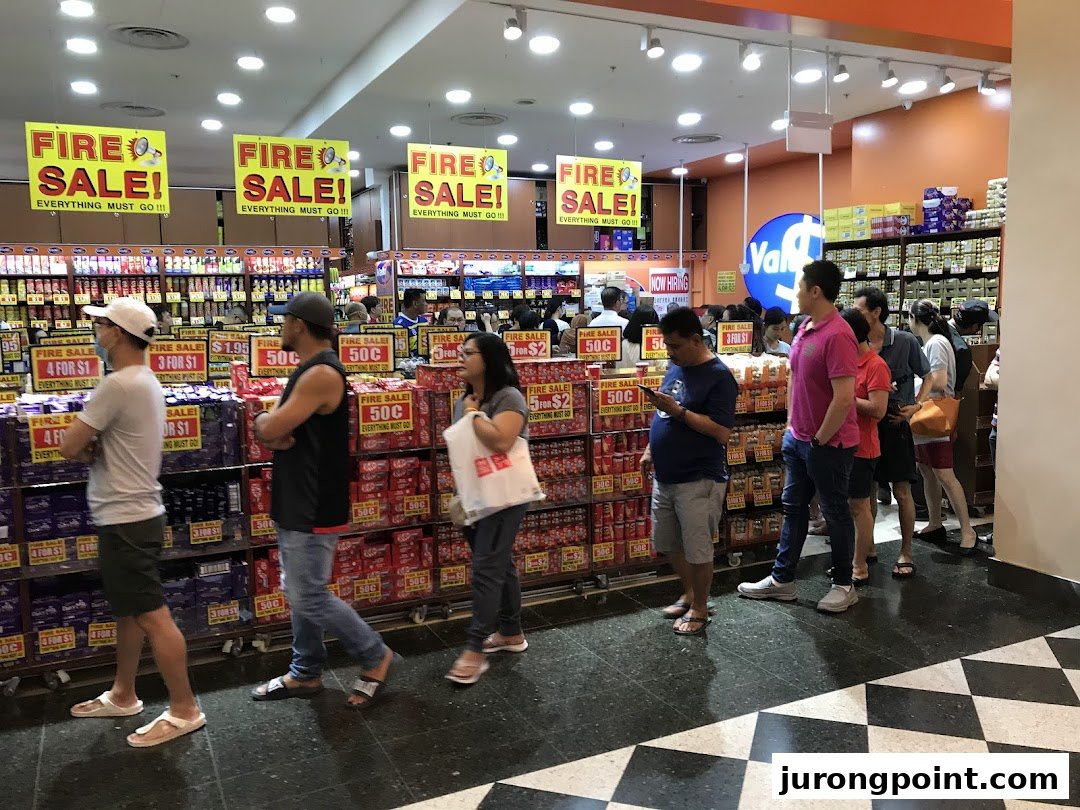 Customers queue at the entrance of Valu, a busy discount store featuring prominent 'Fire Sale' signs.
