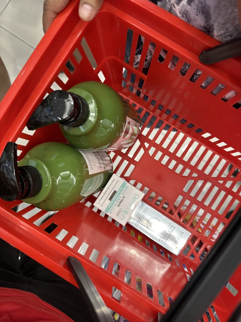 A red shopping basket filled with beauty products, including large green pump bottles and skincare items.