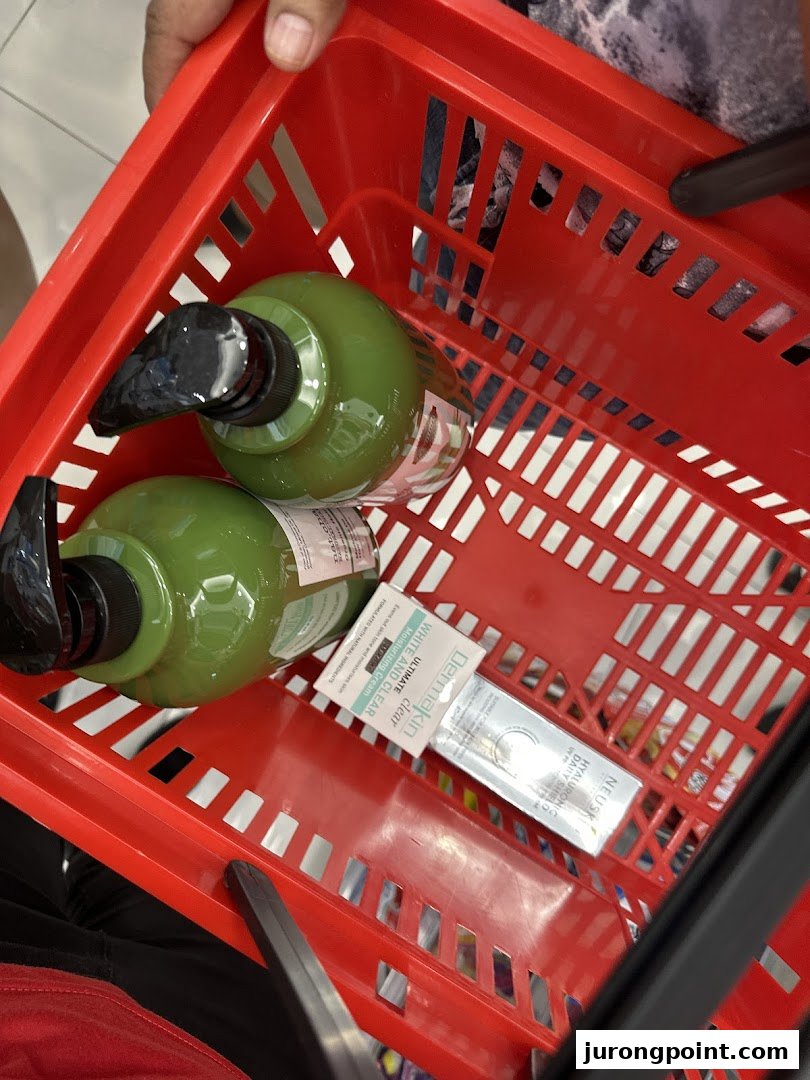 A red shopping basket filled with beauty products, including large green pump bottles and skincare items.