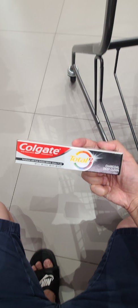 A person holds a box of Colgate Total 12 Charcoal Deep Clean toothpaste inside a store.