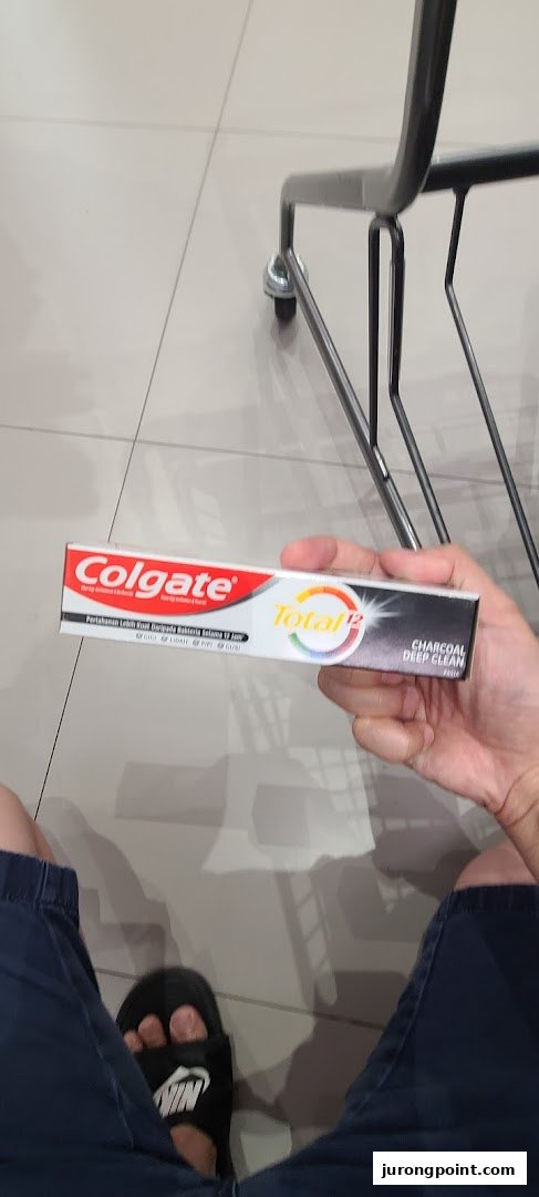A person holds a box of Colgate Total 12 Charcoal Deep Clean toothpaste inside a store.