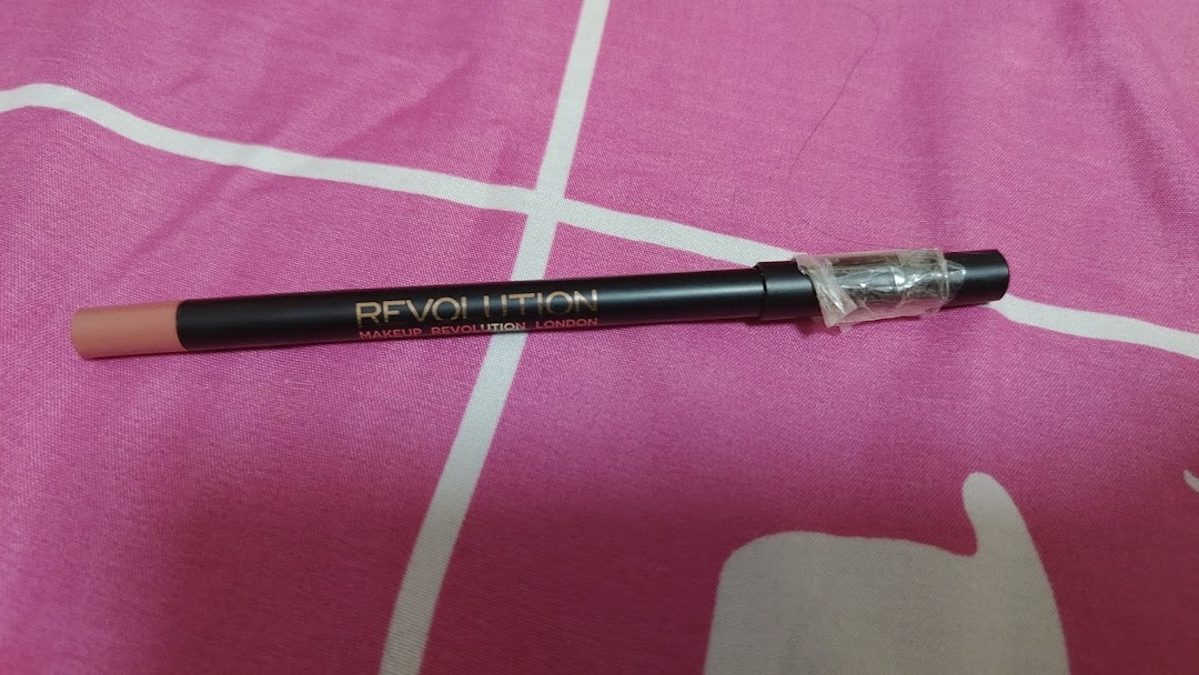 A black Makeup Revolution London pencil with a nude tip on a pink patterned surface.