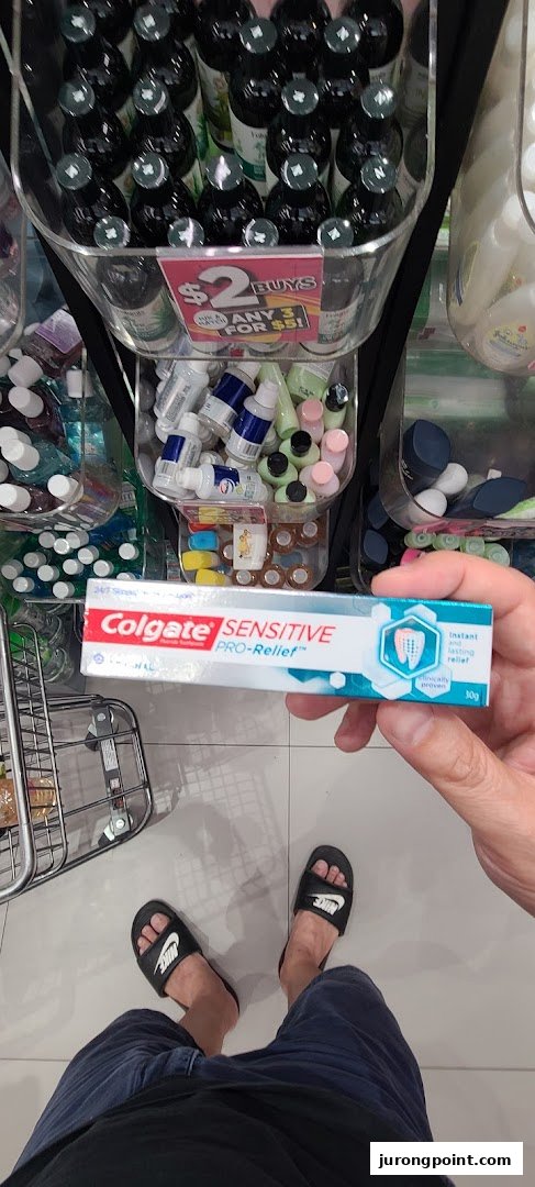 A person holds Colgate Sensitive Pro-Relief toothpaste inside a Watsons store, showcasing various health and beauty products.