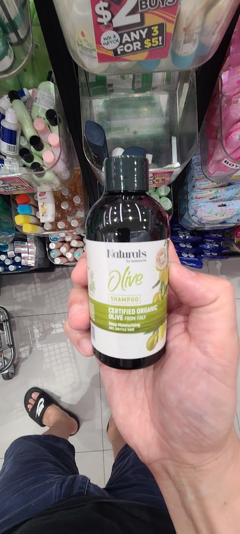 A hand holds a Watsons Naturals Olive Shampoo bottle, showcasing a product inside the store.