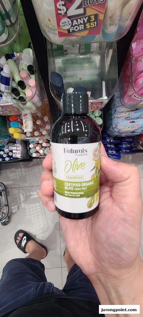 A hand holds a Watsons Naturals Olive Shampoo bottle, showcasing a product inside the store.