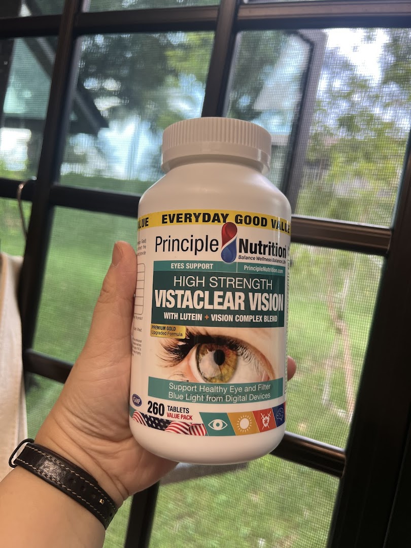 A hand holds a bottle of Principle Nutrition Vistaclear Vision eye support supplements.