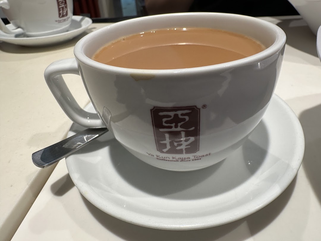 A close-up of a warm beverage in a white Ya Kun Family Cafe cup with its distinctive logo.