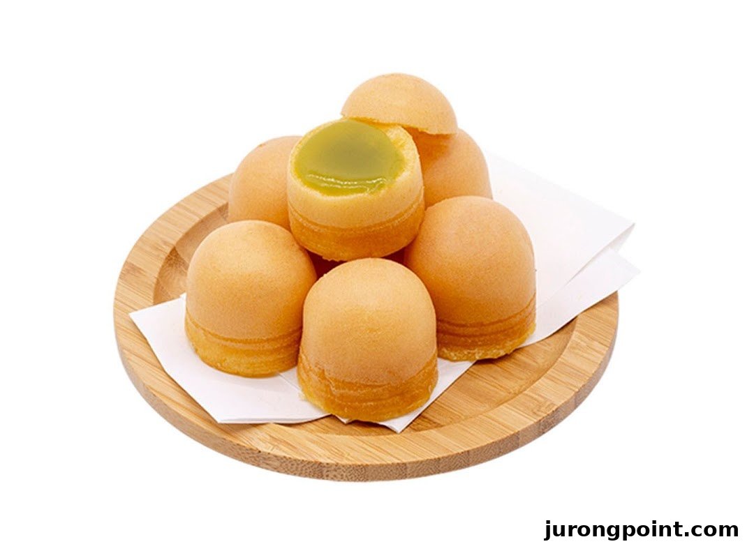 A wooden plate holds several golden-brown pastries, one revealing a vibrant green pandan kaya filling.