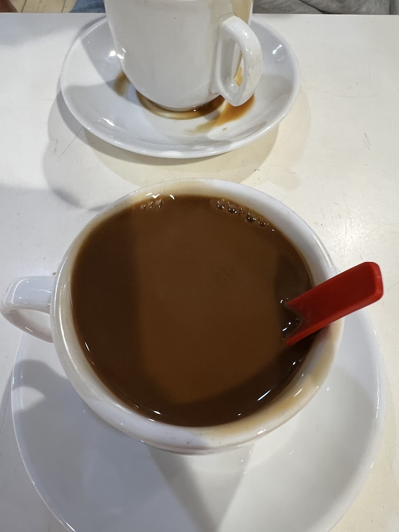 Two cups of traditional coffee or tea, one with a red spoon, on a white table.