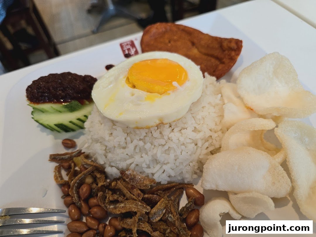 A delicious plate of Nasi Lemak with rice, egg, sambal, anchovies, peanuts, and crackers.