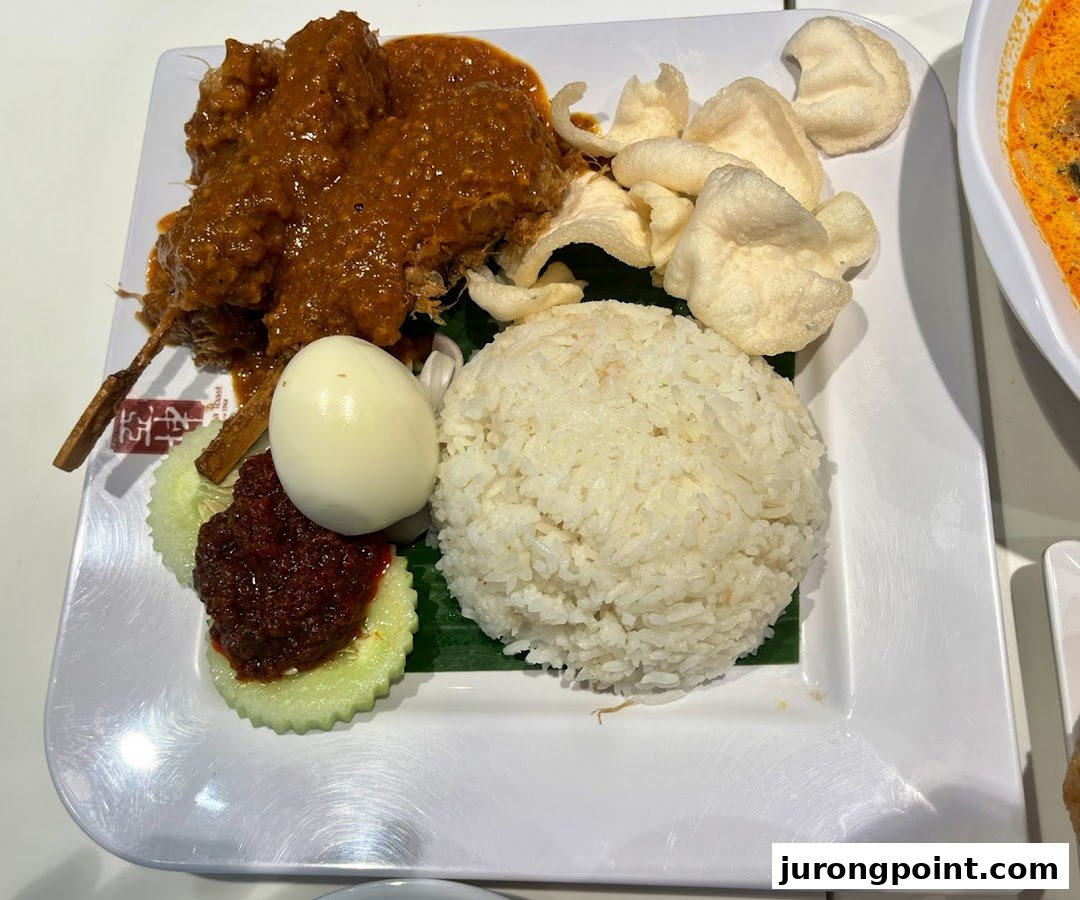 A delicious plate of Nasi Lemak with chicken rendang, fragrant rice, egg, sambal, and crispy keropok.
