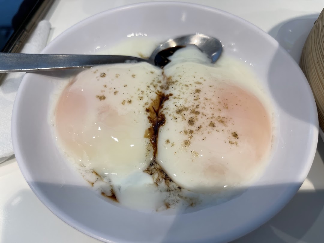 A close-up of two perfectly soft-boiled eggs with soy sauce and pepper in a white bowl.