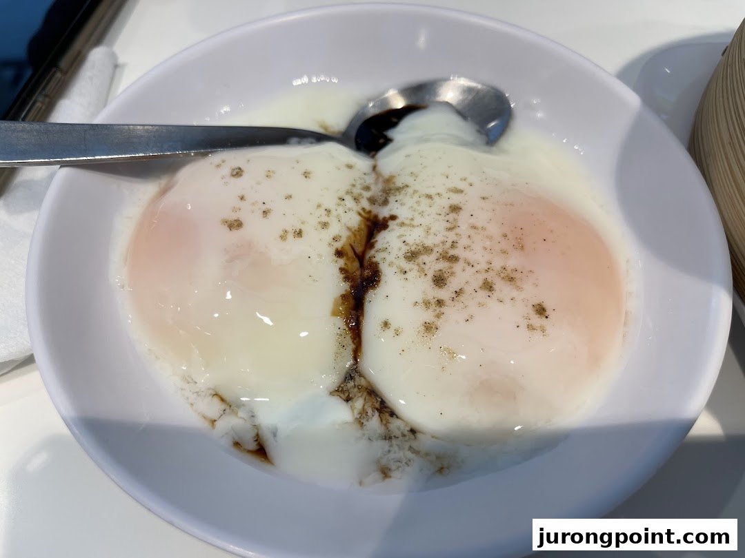 A close-up of two perfectly soft-boiled eggs with soy sauce and pepper in a white bowl.