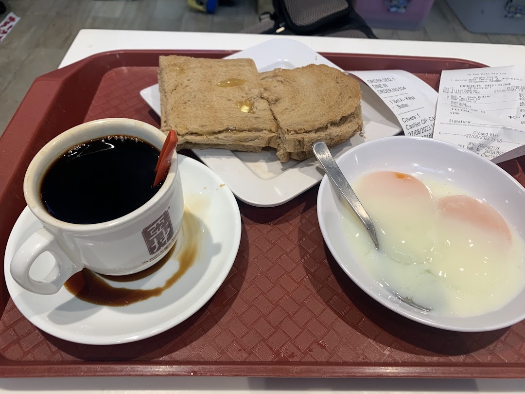 A traditional Singaporean breakfast set featuring coffee, kaya toast, and soft-boiled eggs on a tray.
